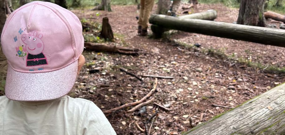 Ei jente med ryggen til ser på ein mann og ein gut som balanserer på ein trestokk i skogen