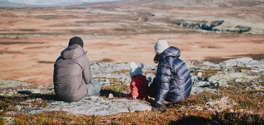 To voksne og et barn som sitter på en stein i fjellet. 