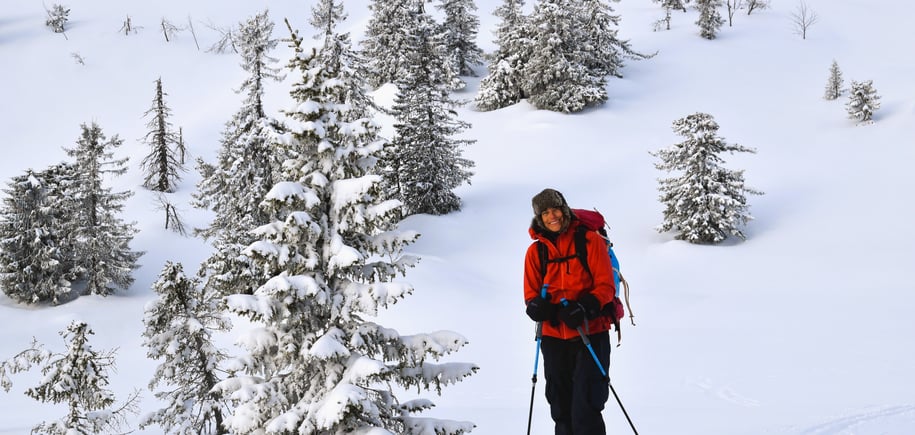 Kvinne i rød jakke står i hvitt snøkledd landskap med ski på beina.