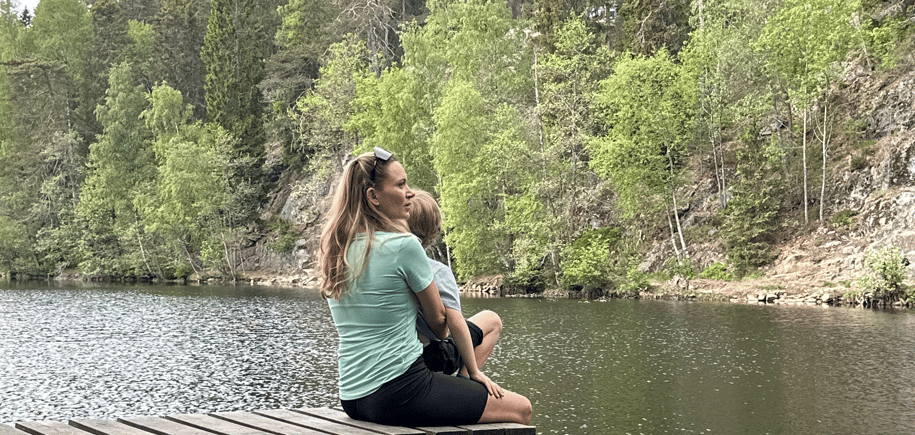 en mor og et barn på en bryggekant ved et skogsvann
