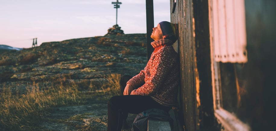 Mann i rød genser som sitter med solen i hytteveggen