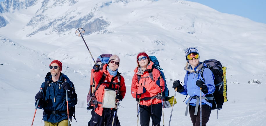 Gruppe på ski blant snøkledde fjell.