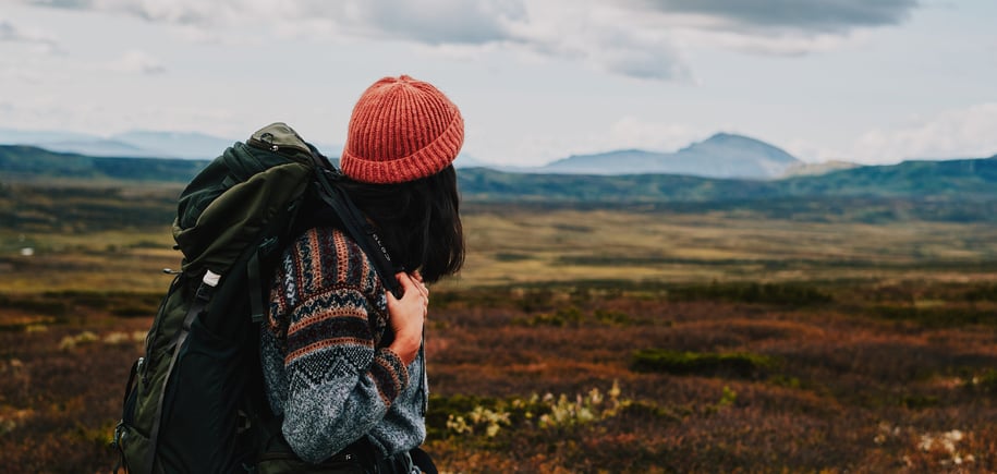 Person med sekk og oransje lue som ser utover fjellet