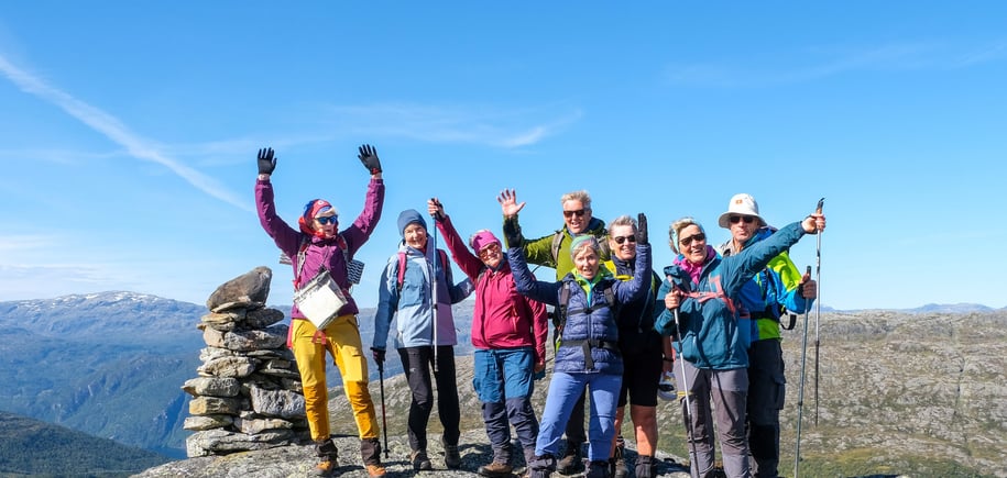 Gjeng glade turgåere med hendene i været på toppen av et fjell.