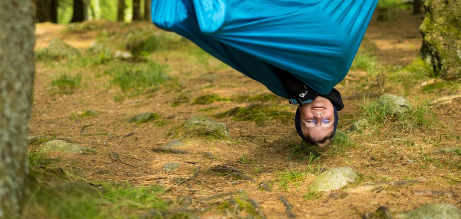 En gutt henger opp ned i hengekøye.