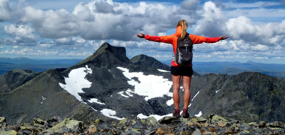 Person står med armene utstrakt og ser vekk fra oss, ut over steinete fjell-landskapet foran oss. 