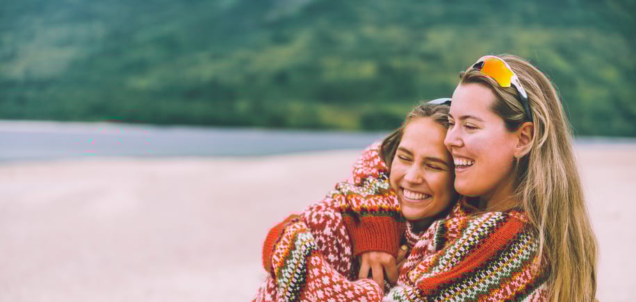 To jenter holder rundt hverandre på strand i fjellet