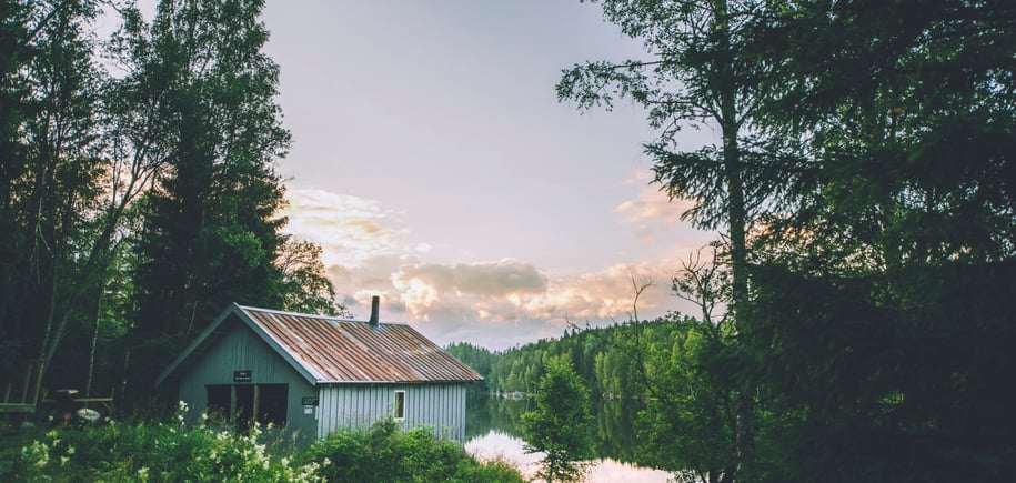 Grå hytte ved vann i skogen
