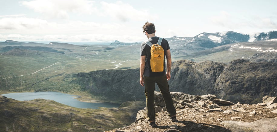 Person står med sekk på ryggen og ser utover vakkert fjellområde