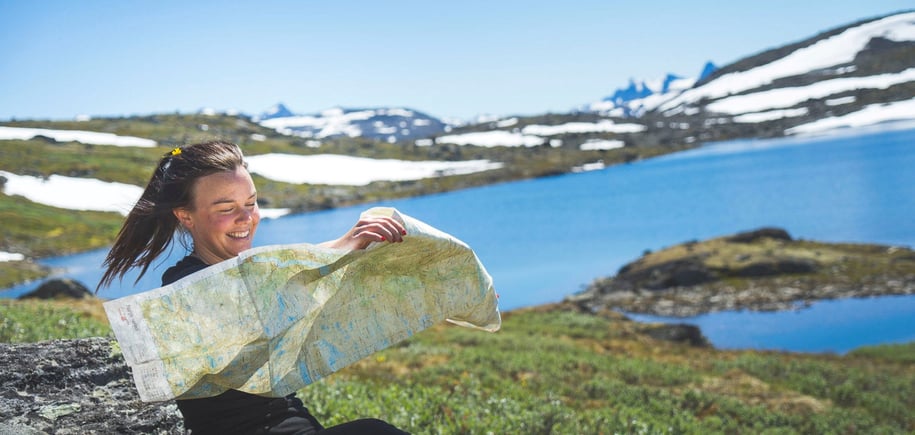 Dame sitter i lyngen og holder kart 