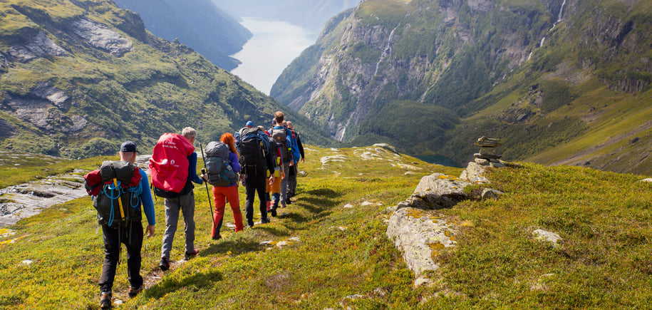 Rekke turgåere på sti ned en dal mot fjorden