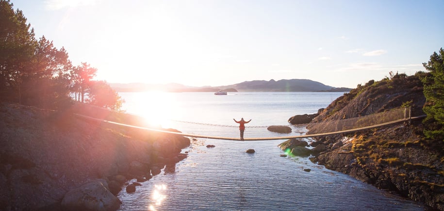 Dronebilde av hengebru på Vassøy i Stavanger. En person står i midten av broen og strekker armene ut.