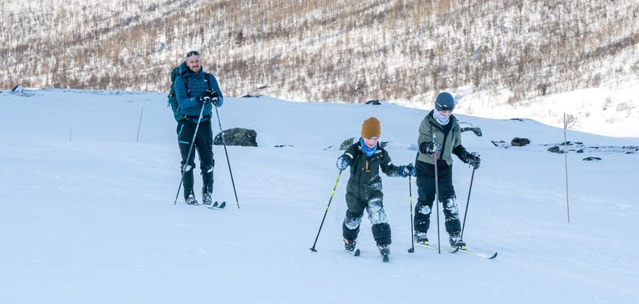 To barn og en voksen som går på ski i fjellet
