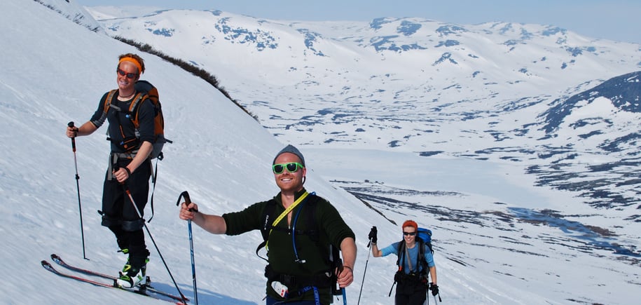 Gjeng på vei opp fjell med shorts og randoneeski.