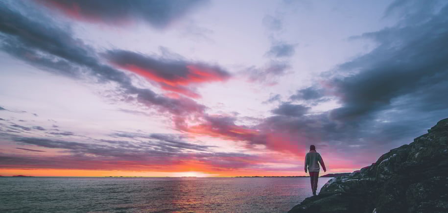 en person som står på en klippe og ser på solnedgangen