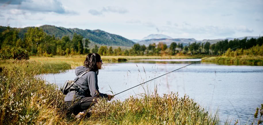 Kvinne med fiskestang i fjellandskap