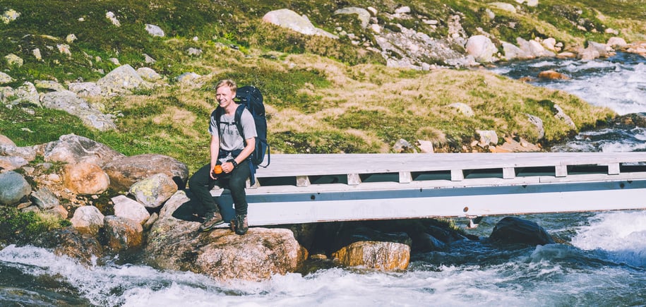 En person som sitter på en bro ved en elv i fjellet