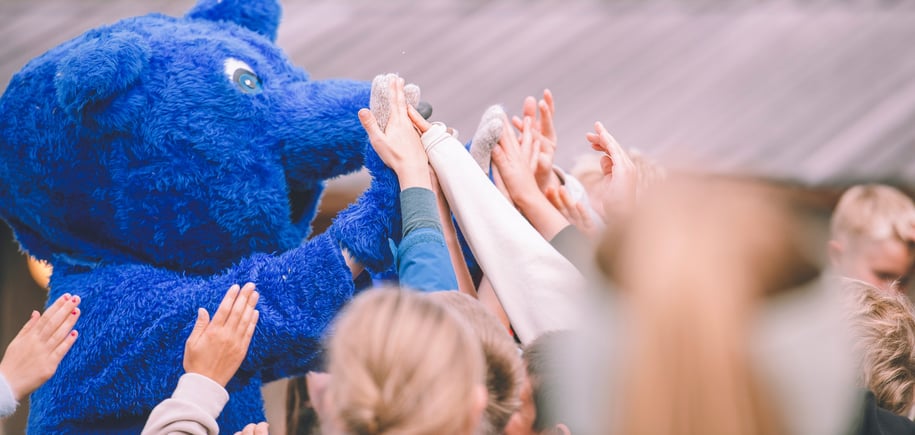 Turbo, en blå maskot gir high five til flere barn.