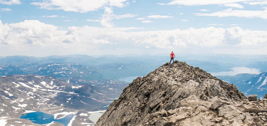 Mann som står på toppen av en fjelltopp og ser utover.