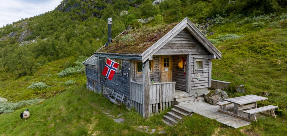 Koselig klassisk hytte med torvtak og norsk flagg utenfor.