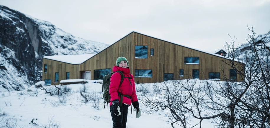 En jente med rød jakke står foran en helt ny hytte.