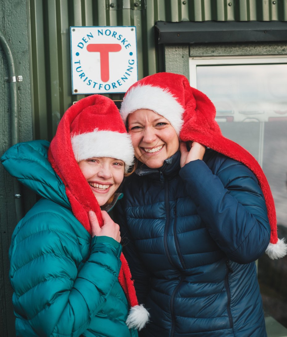 To personer med nisselue utenfor hytte med turistforeningens logo