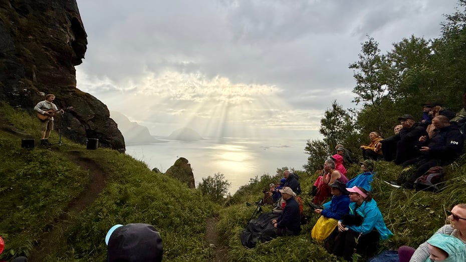 Artisten Moddi spiller gitar foran publikum. Fantastisk utsikt mot vill natur, havet og dramatiske skyer i bakgrunnen
