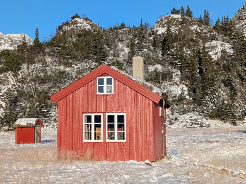 Kvanndalen. Rød hytte bader i sol. Det er litt snø på bakken. 