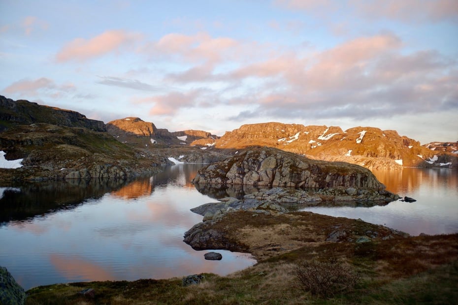 Morgenstemning med soloppgang over et stille vann i fjellet. Det ligger litt snø enkelte steder 