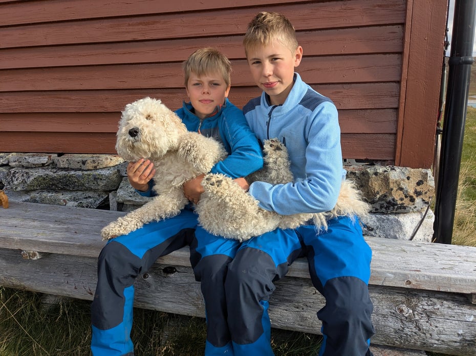 To blåkledde gutter på en benk med en hvit hund på fanget