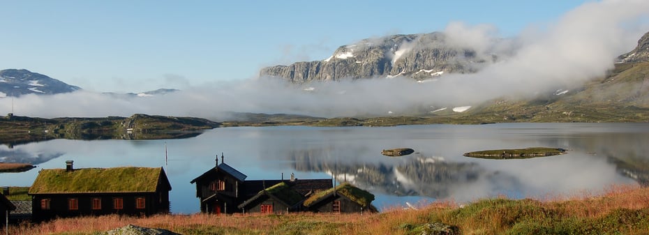 Foto. Haukeliseter fjellstue med fjell og Ståvatn i bakgrunnen.