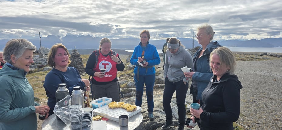 Åtte personer rundt ei siktskive på Keiservarden. En med DNT-vest. Fin utsikt mot havet