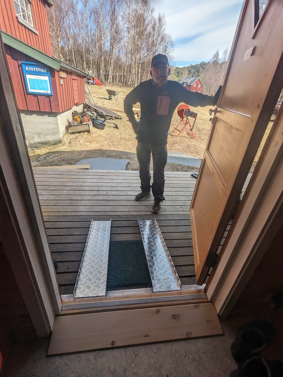 Mann viser fram rullestolrampe inn til hytte