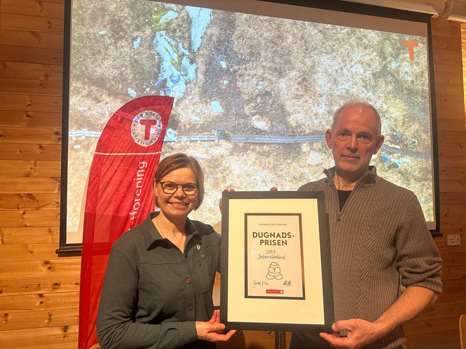 Jostein Nordland mottar diplom for dugnadsprisen 2024 fra styreleder Gunhild Holtet Eie. I bakgrunnen vises en presentasjon i anledning prisutdelingen.