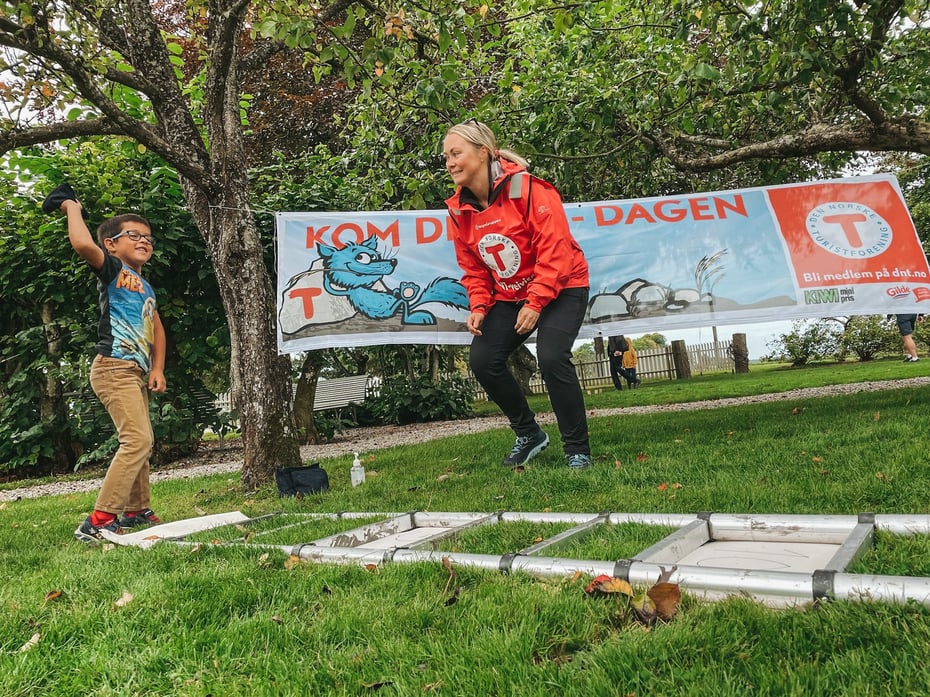 En voksen i rød DNT-vest hjelper et barn med en aktivitet under Kom deg ut dagen.