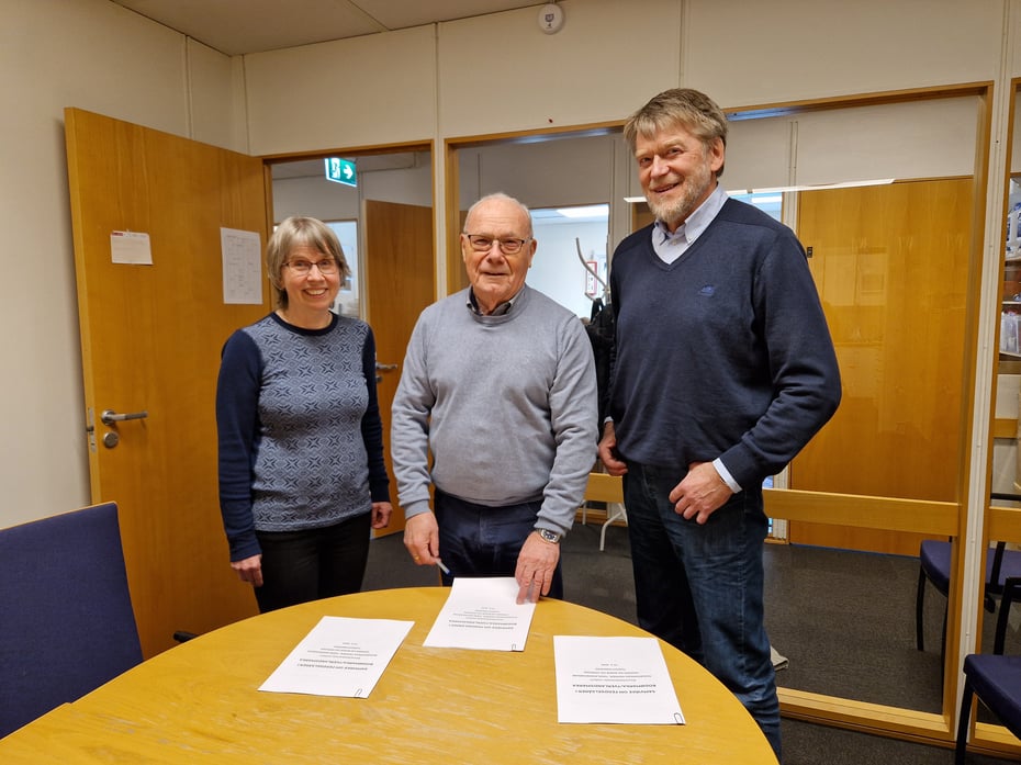 Tre personer som gjør seg klar til å underskrive dokumenter som ligger på et bord