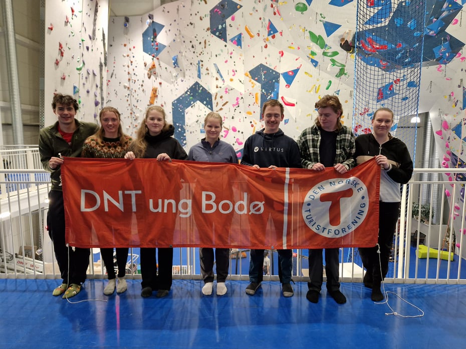 7 ungdommer står på rekke i en klatrehall. De holder et banner der det står DNT ung