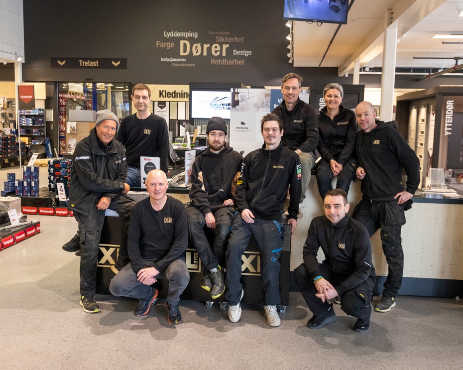 Ni blide selger samlet rundt en disk hos XL-bygg. Kledd i svart. En dame.