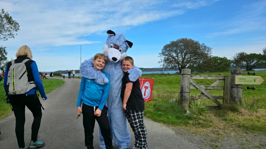 To gutter står med svær, blå maskot som ser ut som en rev. De klemmer.