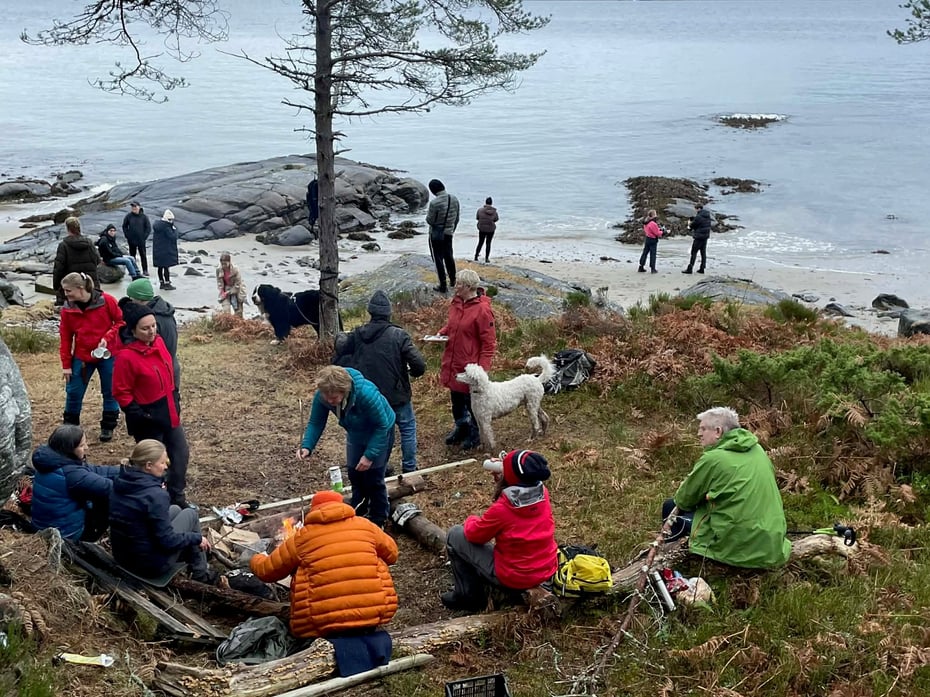 Gruppe personer på tur brenner bål og spiser pepperkaker i nærheten av sjøen
