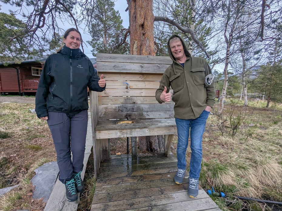 En mann og ei dame viser tommel opp for en vannpost