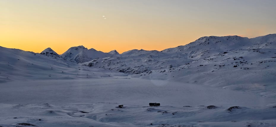 Snødekte vinterfjell med sol som lyser opp i bakgrunnen, men som ligger bak fjellene