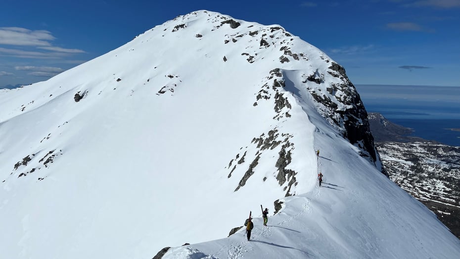 Personer går på eggen av en snødekt topp for skikjøring