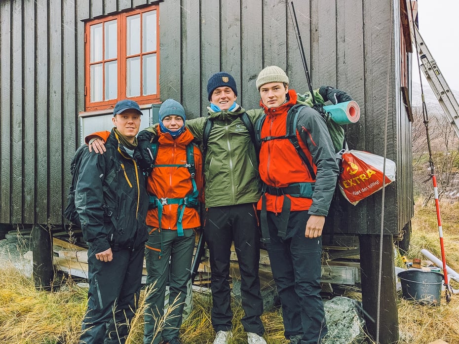 Fire studenter som står og holder rundt hverandre mens de smiler til kameraet forran DNT-hytta.