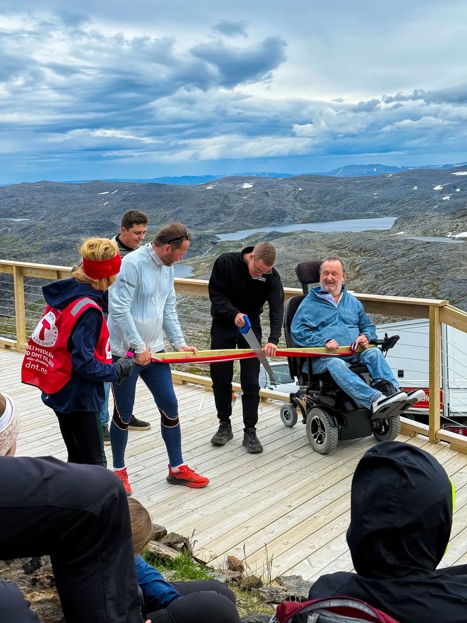 En man sager av en planke sammen med en yngre gutt og en man i rullestol