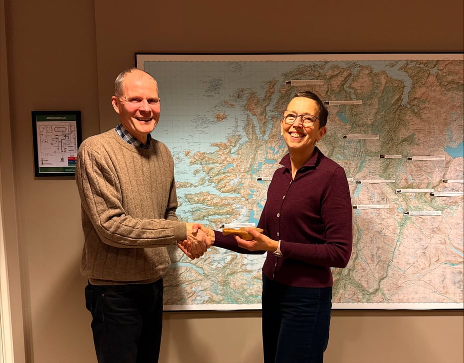 En mann og ei dame tar hverandre i handa, og hun holder en trekopp. Kart i bakgrunnen. 