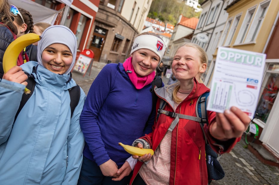 Tre jenter som smiler til kamera og holder opp et OPPTUR startkort