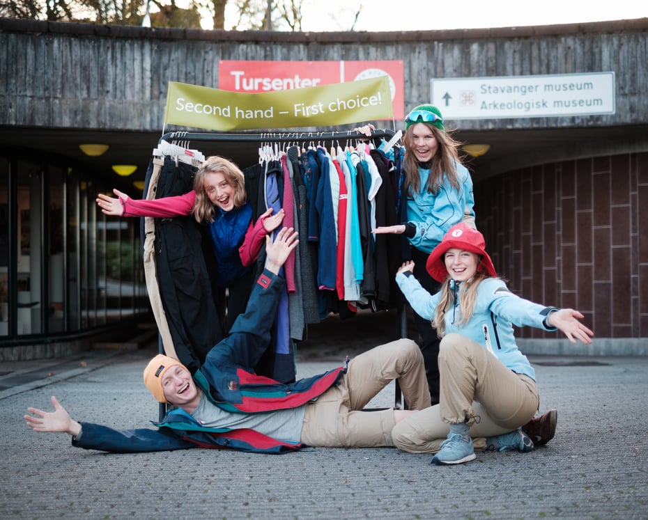 Fire ungdommer poserer med et tøystativ med brukte friluftsklær