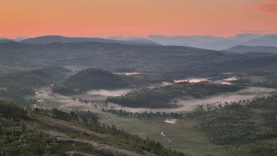 Rolig landskap med tåke i dalene og rød midnattsolhimmel