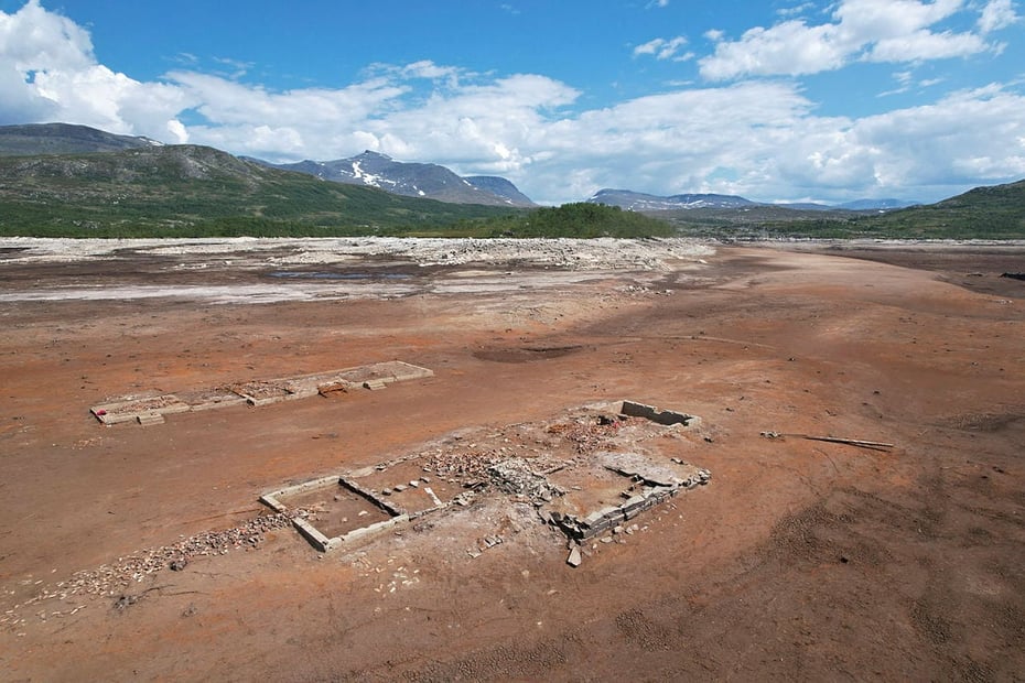 Et dronebilde tatt ovenfra, av den brune og gjørmete bunnen av en innsjø som er tappet ut, hvor ruinene av en grunnmur er synlig.